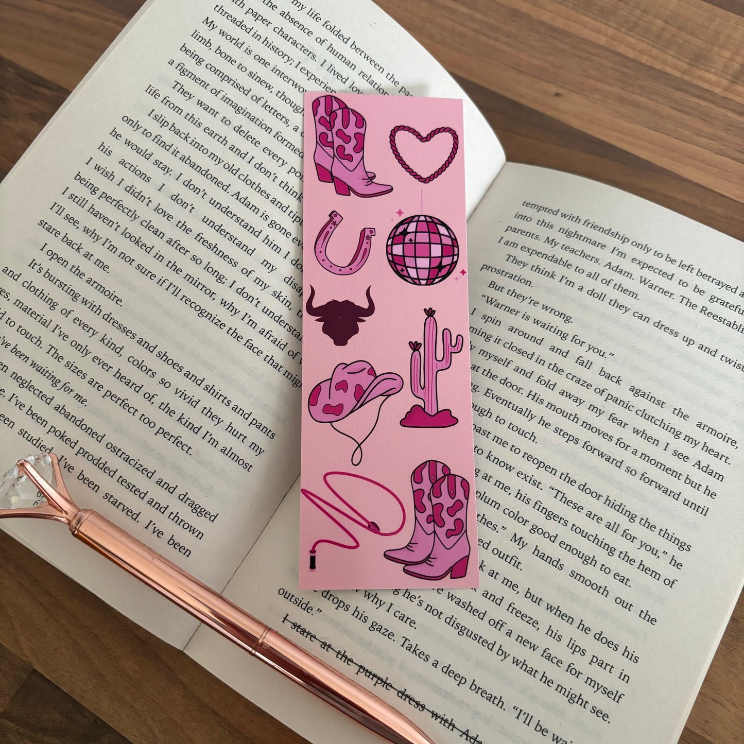 An open book with a pink cowboy bookmark and pen on a desk