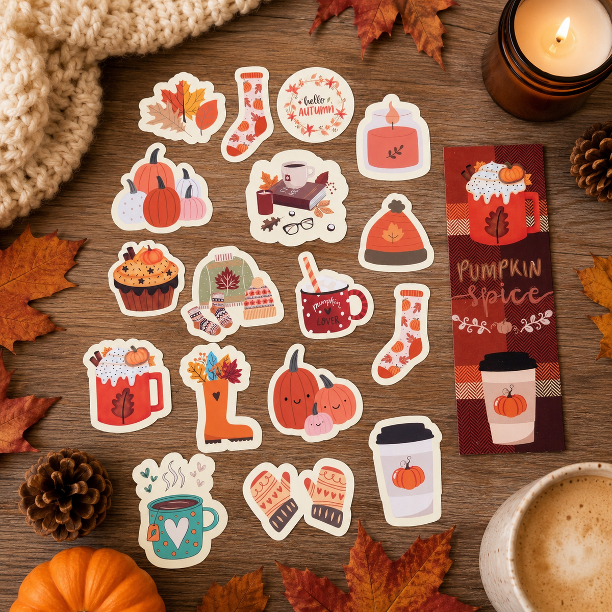 A collection of autumn-themed sticker designs arranged on a wooden tabletop with fall leaves, pinecones, a knitted sweater corner, a lit candle, and a coffee cup. The stickers include pumpkins, boots, mugs, socks, hats, and a bookmark-style design reading 'Pumpkin Spice'.