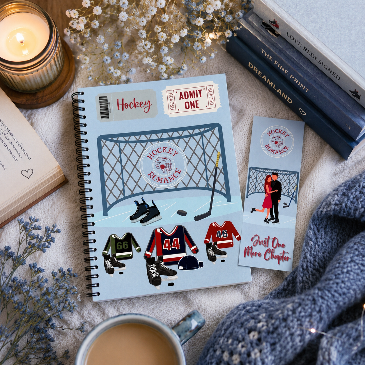 A styled flat-lay featuring a spiral-bound notebook and matching bookmark with ice hockey-themed illustrations, including a goal net, skates, jerseys, and phrases like 'Hockey Romance' and 'Just One More Chapter.' The scene includes a lit candle, books, dried flowers, a mug of coffee, and a chunky knit sweater on a soft fabric surface.