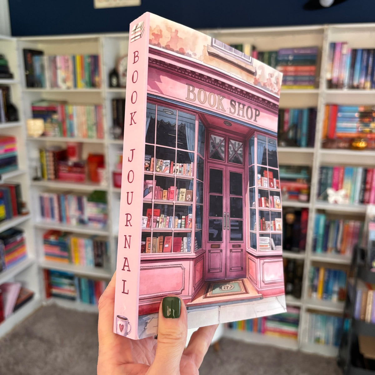 Book Journal with a pink bookshop design held in front of a bookshelf.