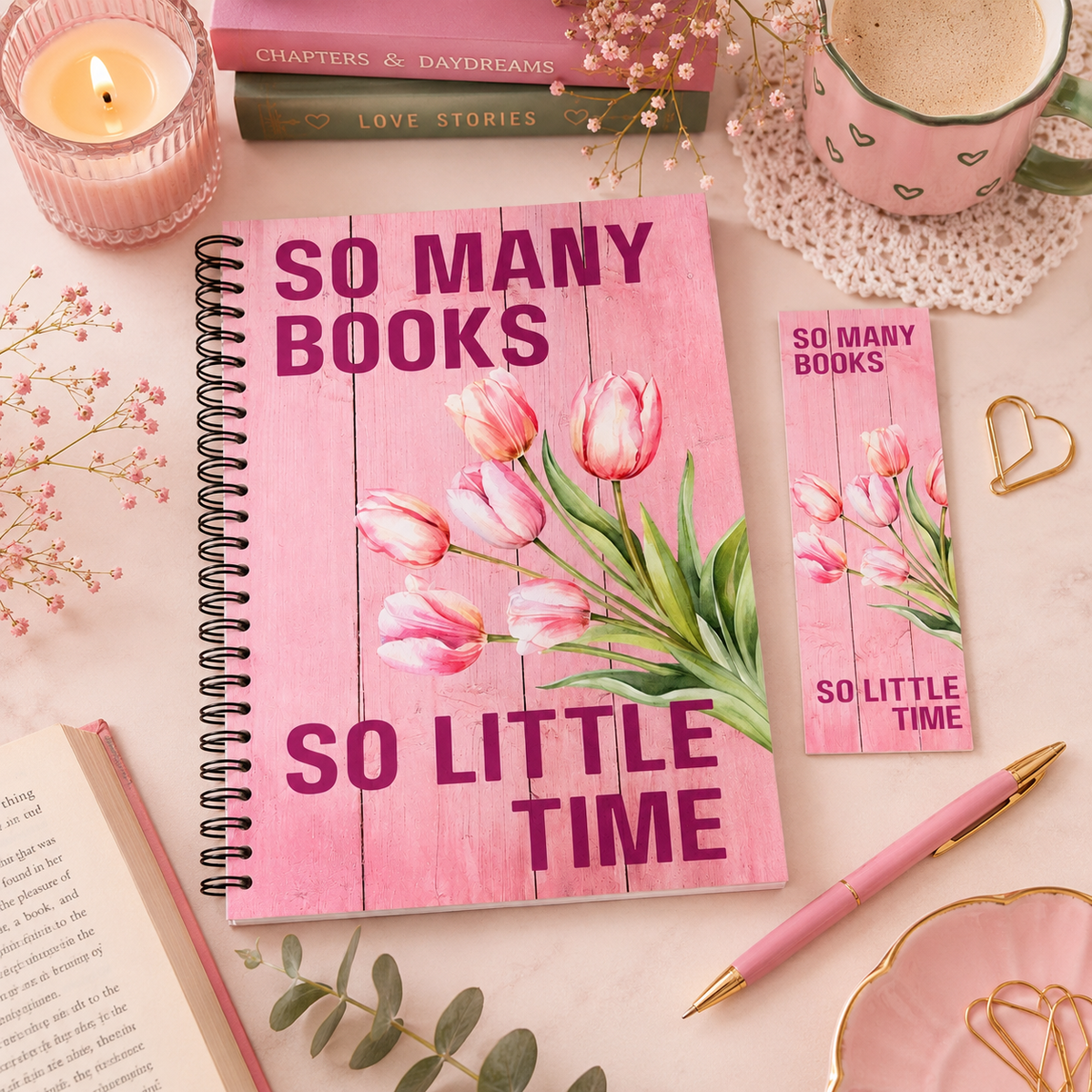 A pink spiral reading journal with a matching bookmark and pen, styled on a light pink surface with a candle, mug, books, and floral accents. The notebook cover features a pink wood-plank design with pink tulips and the text 'SO MANY BOOKS SO LITTLE TIME'. in the style of the book It Ends With Us.