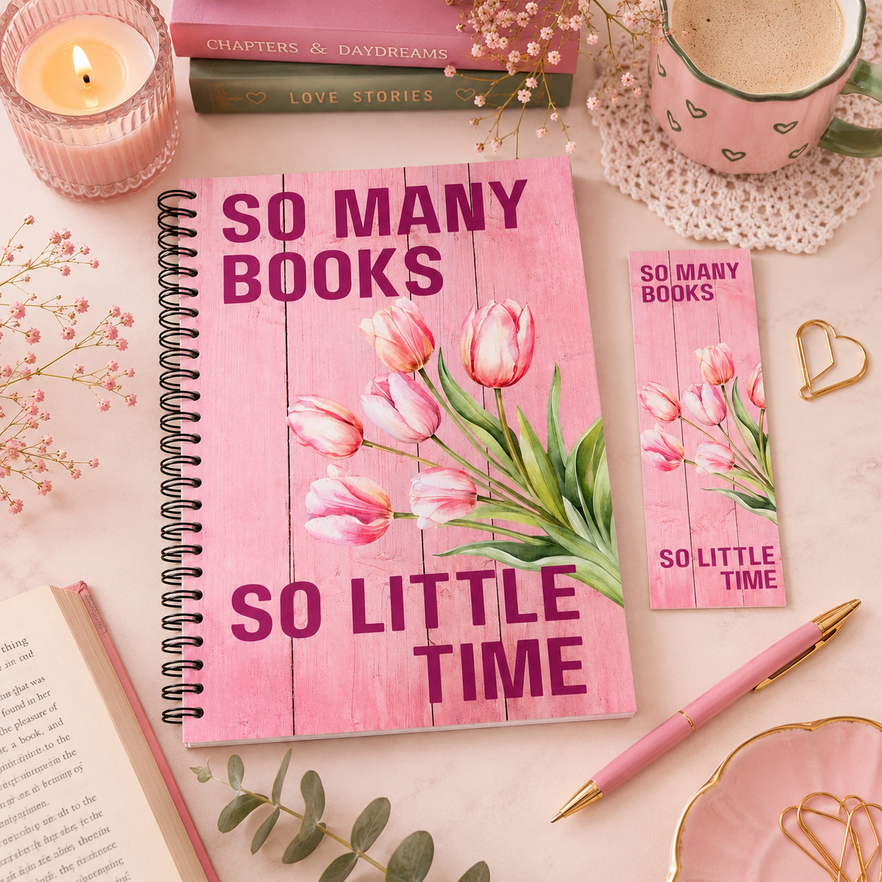 A pink spiral reading journal with a matching bookmark and pen, styled on a light pink surface with a candle, mug, books, and floral accents. The notebook cover features a pink wood-plank design with pink tulips and the text 'SO MANY BOOKS SO LITTLE TIME'. in the style of the book It Ends With Us.