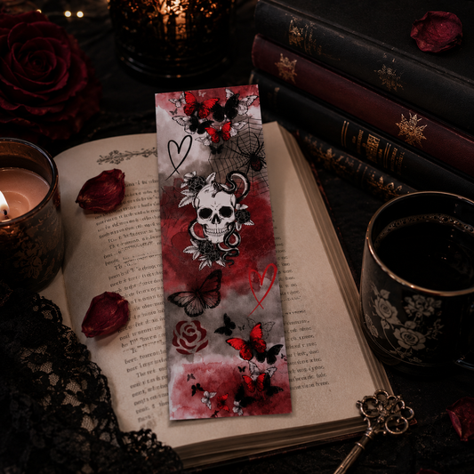 A gothic-style bookmark featuring a skull, roses, butterflies, and hearts, displayed on an open book surrounded by candles, rose petals, and old books.